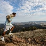 A man jogging on a scenic mountain trail, surrounded by vast landscapes under a clear sky.