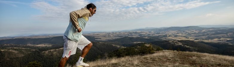 A man jogging on a scenic mountain trail, surrounded by vast landscapes under a clear sky.