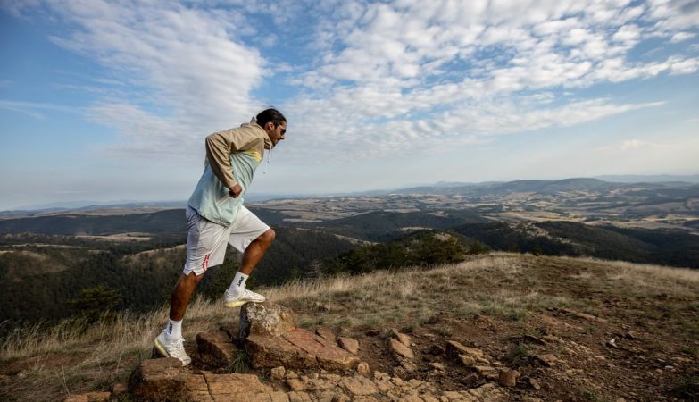 A man jogging on a scenic mountain trail, surrounded by vast landscapes under a clear sky.